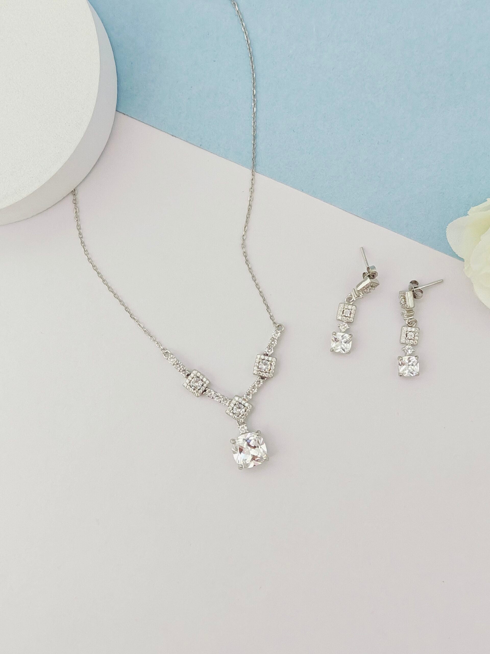 Silver necklace and earrings on a light blue and white background